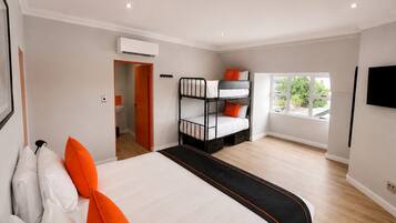 A hotel room with a large bed, a bunk bed, a window with a view, and a flat-screen TV.