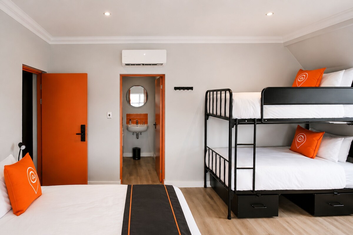Ett hotellrum med en våningssäng, en enkelsäng, ett badrum med handfat och en luftkonditioneringsanläggning.
