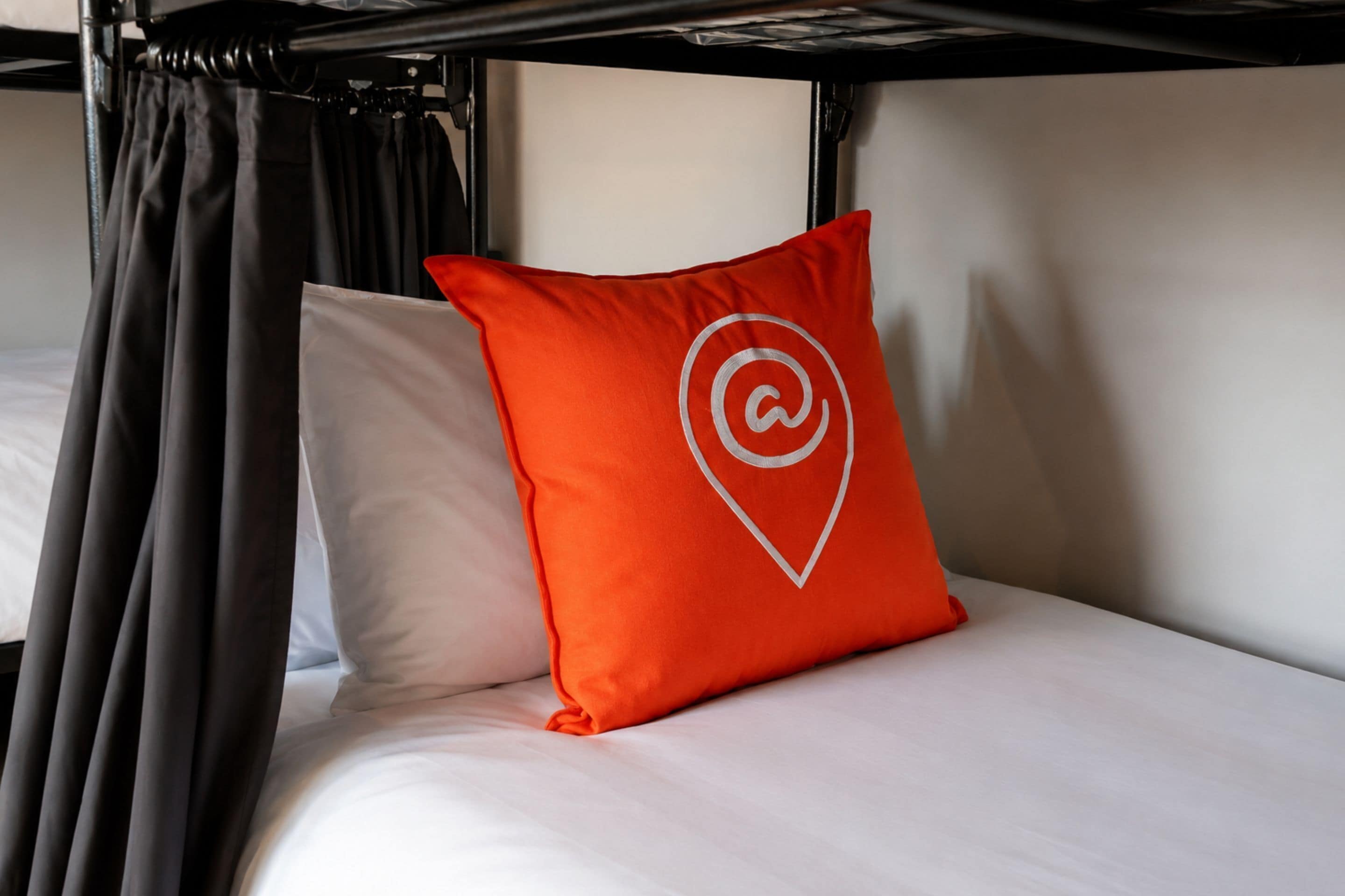 A bunk bed with a white mattress and a red pillow with a white logo.