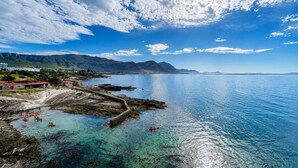 Een kustlandschap met helderblauw water, rotsachtige oevers en bergen in de verte.