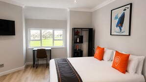 Een hotelkamer met een bed, een bureau, een stoel, een televisie en een raam met uitzicht op bomen.
