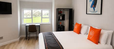 A hotel room with a bed, a desk, a chair, a TV, and a window with a view of trees.