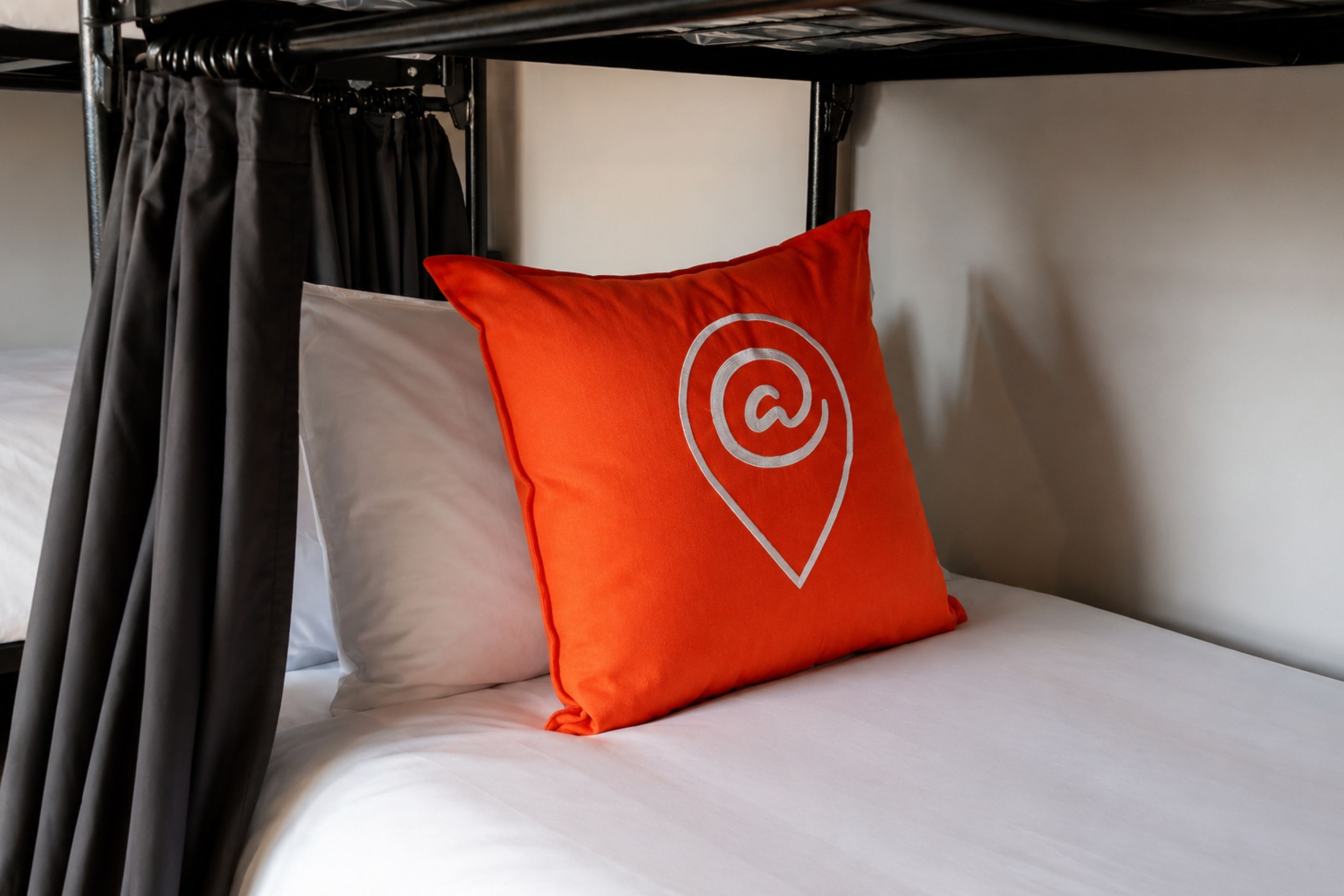 A bunk bed with a white mattress and a red pillow with a white logo.