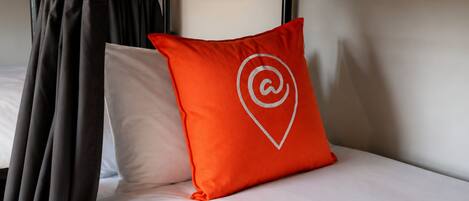 A bunk bed with a white mattress and a red pillow with a white logo.