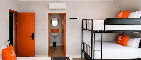 A hotel room with a bunk bed, a single bed, a bathroom with a sink, and an air conditioning unit.