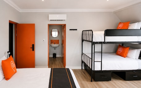 A hotel room with a bunk bed, a single bed, a bathroom with a sink, and an air conditioning unit.