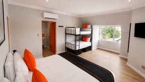 A hotel room with a large bed, a bunk bed, a window with a view, and a flat-screen TV.