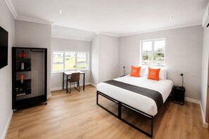 Ett hotellrum med en säng, ett skrivbord, en stol, en garderob och ett fönster.