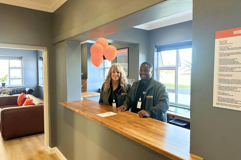 Un comptoir d’accueil avec deux employés, un panneau d’affichage avec du texte et une fenêtre donnant sur l’extérieur.