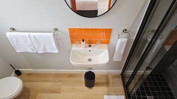 Une salle de bain avec un lavabo blanc, un miroir, des toilettes et un espace douche.