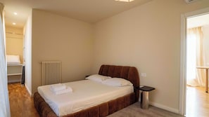 Ein Schlafzimmer mit einem Bett, einem Nachttisch, einem Heizkörper und einer Tür zu einem anderen Raum.