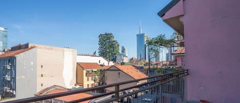 Un paisaje urbano con edificios modernos, un rascacielos destacado y un balcón con barandilla.