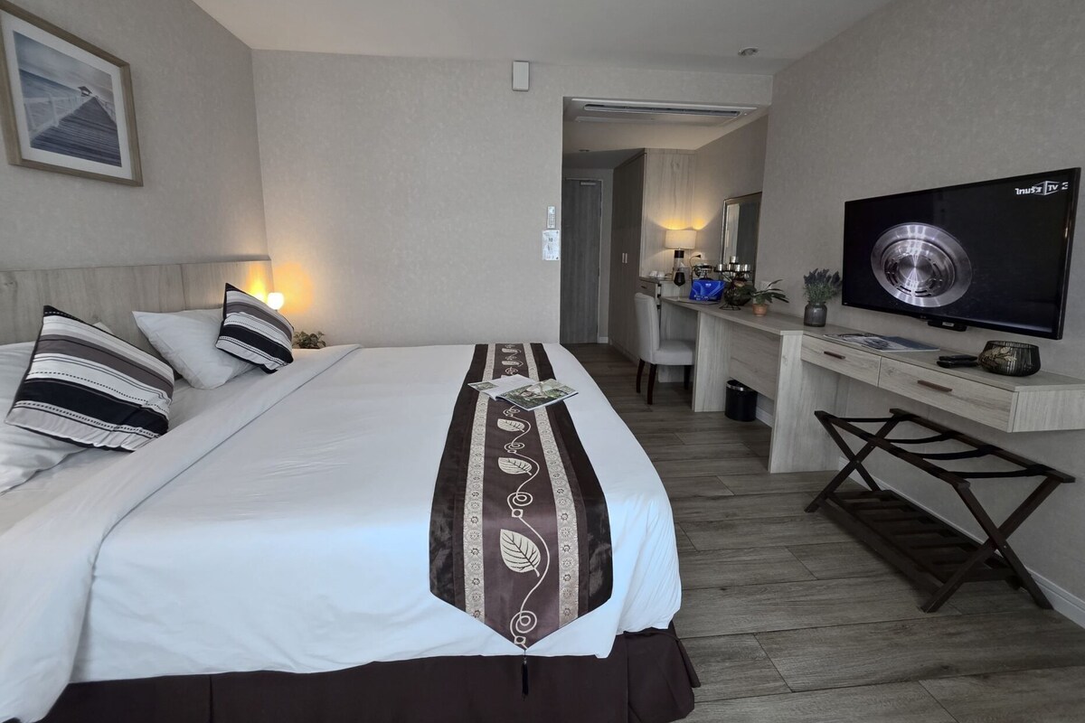 A hotel room with a bed, bedside table, TV, desk, chair, and a framed picture on the wall.