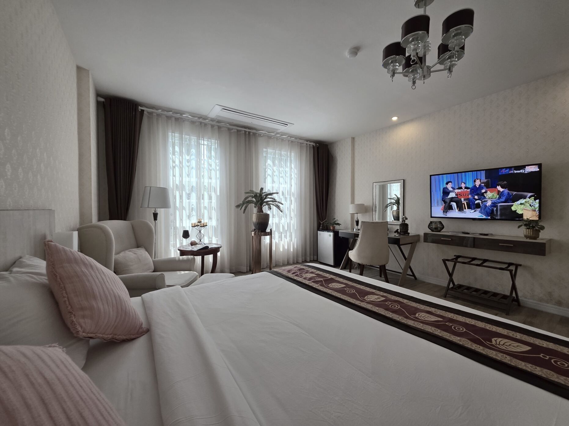 Een hotelkamer met een groot bed, een bureau met stoel, een televisie en een potplant.