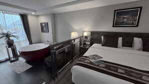 A hotel room with a large bed, a separate bathtub, a bedside table with a lamp, a framed picture on the wall, and a potted plant by the window. - Le Cannes, A Recall Luxe Hotel, Chiang Mai (Chiang Mai)