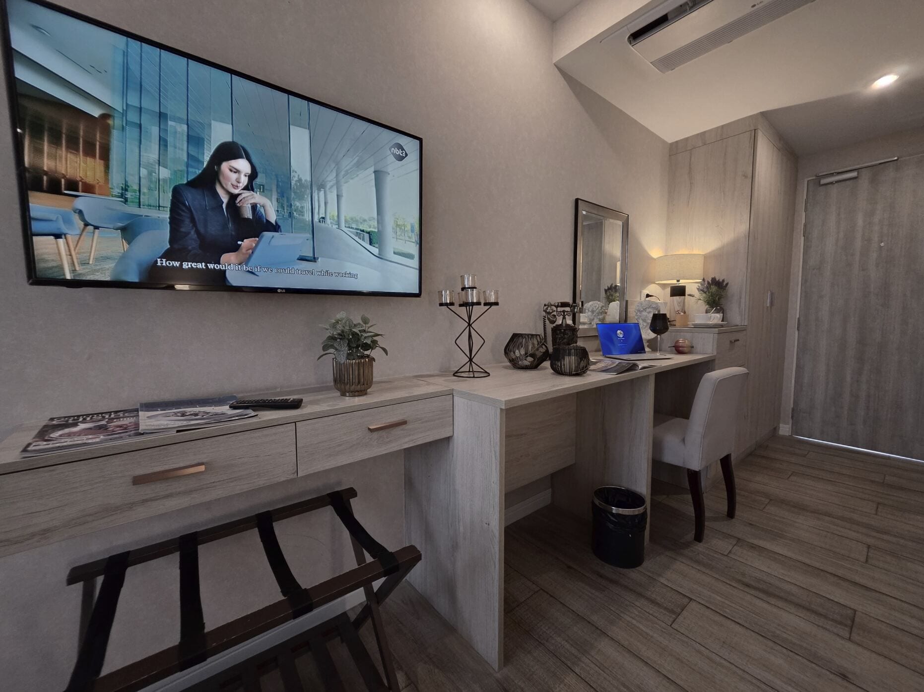 Un espacio de oficina moderno con una televisión de pantalla plana grande, un escritorio con una computadora portátil, una silla, una planta pequeña y un bote de basura.