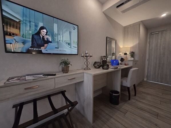 A modern office space with a large flat-screen TV, a desk with a laptop, a chair, a small plant, and a trash can. - Le Cannes, A Recall Luxe Hotel, Chiang Mai (Chiang Mai)