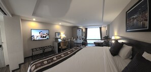 Ett hotellrum med en säng, ett skrivbord, en stol, en tv och utsikt över staden.