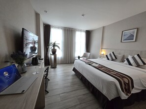 A hotel room with a bed, a desk with a laptop, a TV, a potted plant, and a window with curtains. - Le Cannes, A Recall Luxe Hotel, Chiang Mai (Chiang Mai)