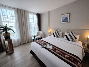 Ett hotellrum med en stor säng, en stol, ett litet bord, en krukväxt och en inramad tavla på väggen.