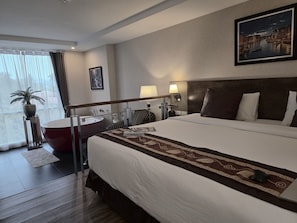 A hotel room with a large bed, a desk, a chair, a potted plant, and a view of a cityscape. - Le Cannes, A Recall Luxe Hotel, Chiang Mai (Chiang Mai)