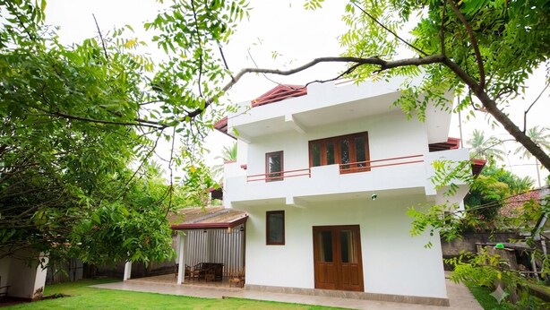 A two-story white building with a balcony, a covered porch, and a well-maintained lawn. - Blue Lotus Yoga House (Hikkaduwa)
