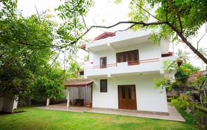 A two-story white building with a balcony, a covered porch, and a well-maintained lawn. - Blue Lotus Yoga House (Hikkaduwa)