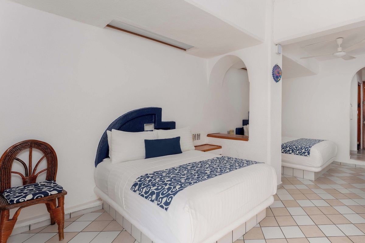 A bedroom with a bed, a chair, a small table, and a wooden door.