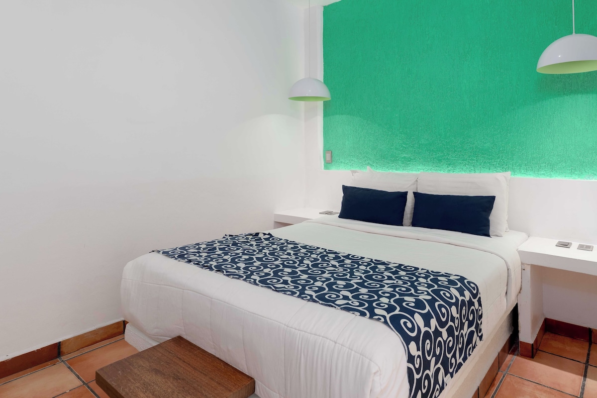 A hotel room with a bed, a nightstand, a window with curtains, and a green wall.
