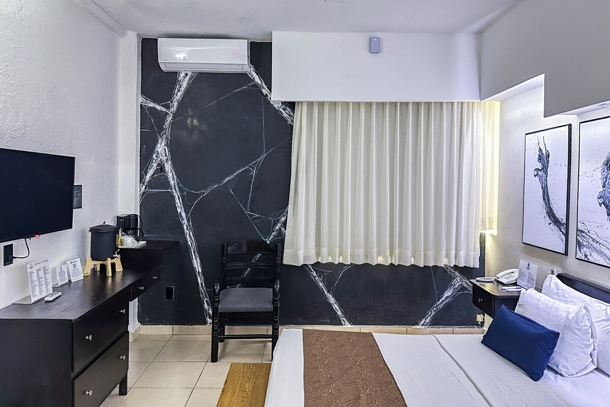 Hotelkamer met een bed, een bureau met computer, een stoel, een televisie en een airconditioner aan de muur.