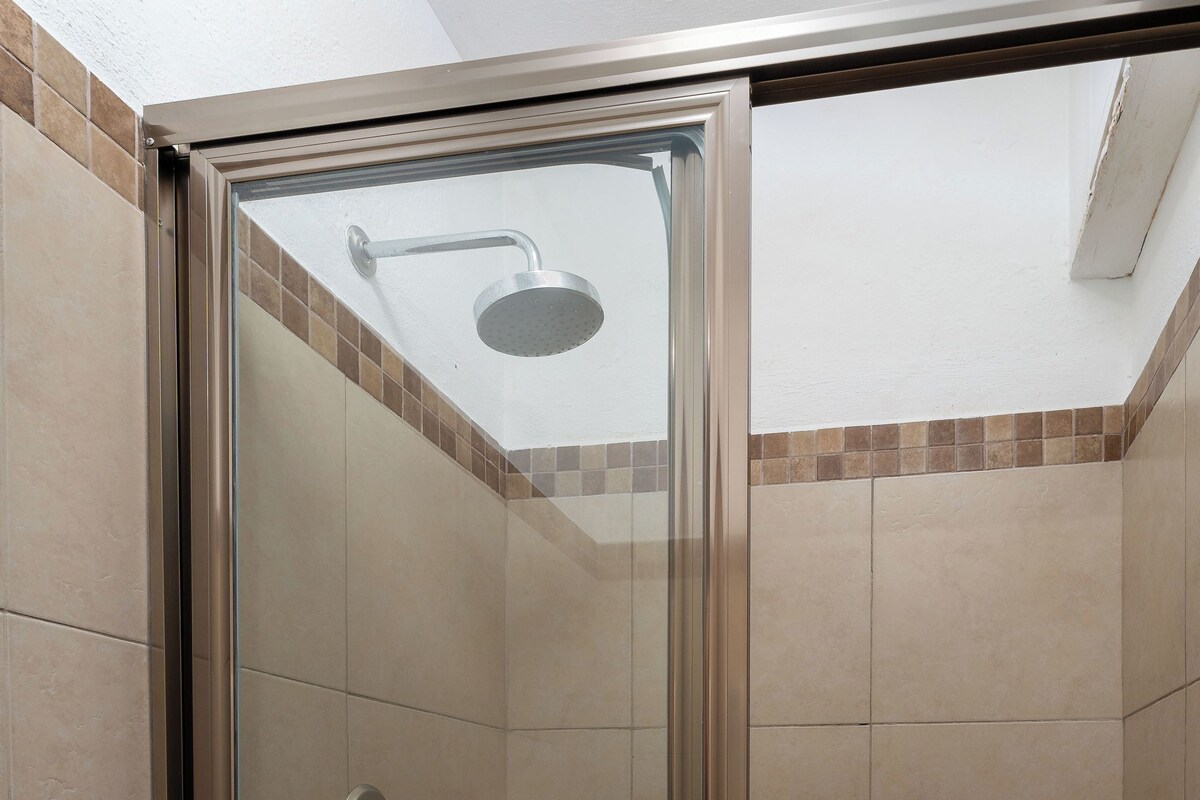 A glass-enclosed shower stall with a handheld showerhead, tiled walls, and a checkered floor pattern.