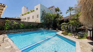 A swimming pool with clear blue water, surrounded by a stone wall and various tropical plants. - Hotel Casa Chahue (Santa María Huatulco)