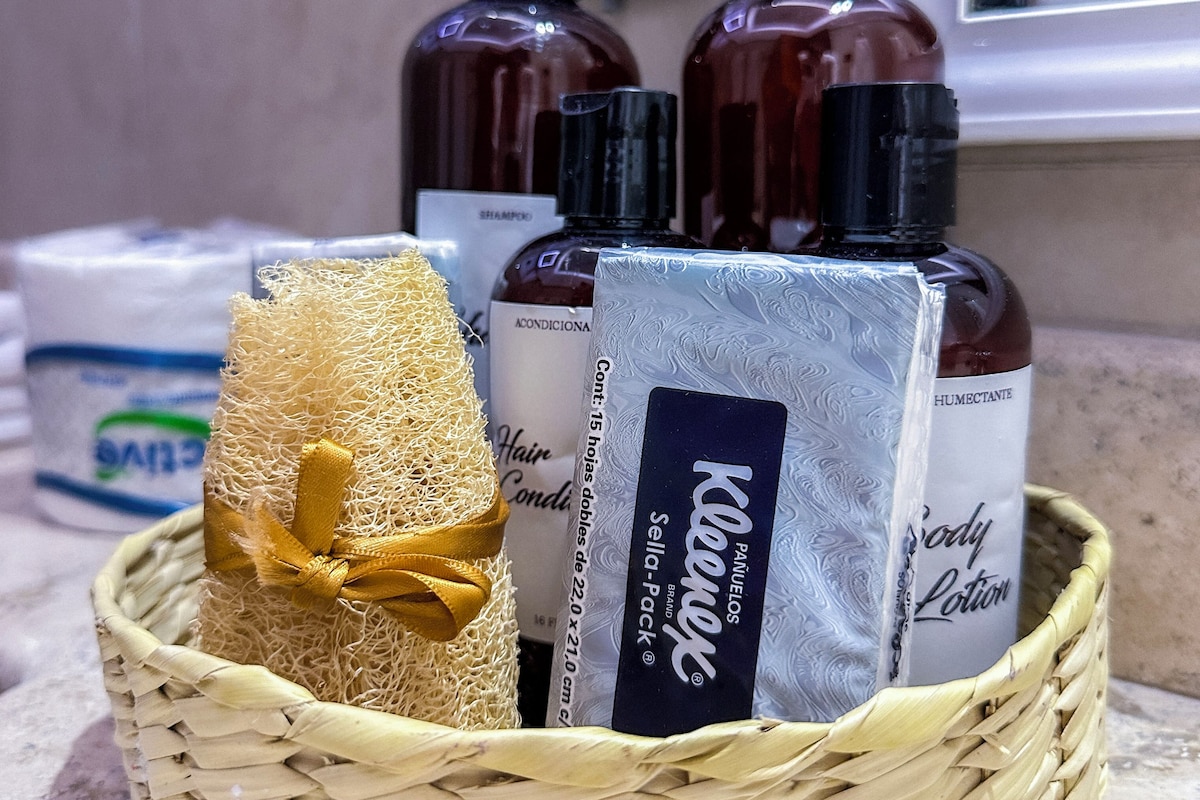 A wicker basket containing a hairbrush, a bottle of shampoo, a bottle of body lotion, and a bottle of conditioner.