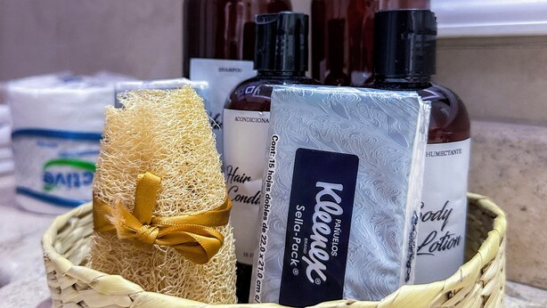 A wicker basket containing a hairbrush, a bottle of shampoo, a bottle of body lotion, and a bottle of conditioner. - Hotel Casa Chahue (Santa María Huatulco)