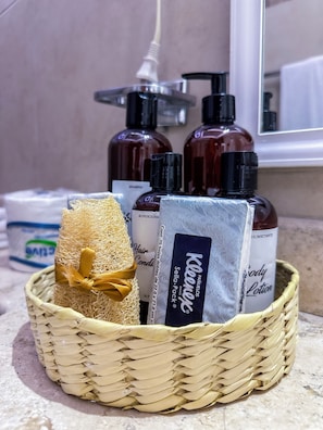Un panier en osier contenant une brosse à cheveux, un flacon de shampoing, un flacon de lotion pour le corps et un flacon d’après-shampoing.