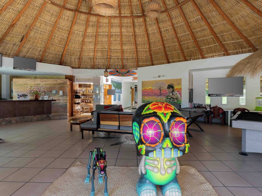 A hotel lobby with a thatched roof, a reception desk, a pool table, and a bar area.