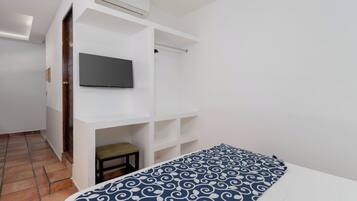 A bedroom with a bed, a TV mounted on a white wall, and a small stool.