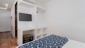 Un dormitorio con una cama, un televisor montado en una pared blanca y un taburete pequeño.