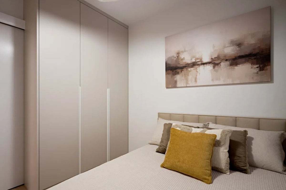 Un dormitorio con cama, almohadas, cabecero, armario y un cuadro en la pared.