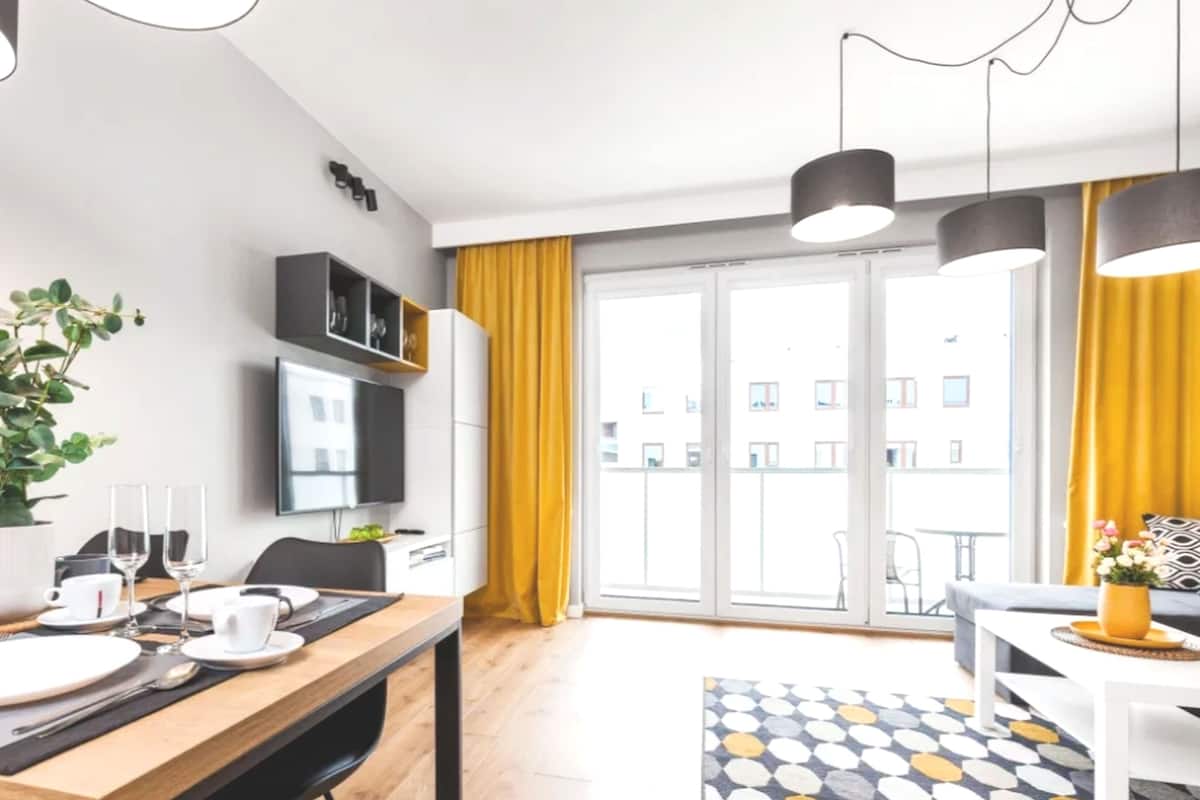 A modern living room with a dining area, large windows, and a view of buildings.