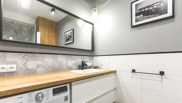 Un baño moderno con tocador de madera, un espejo grande, un lavamanos y ducha de vapor.