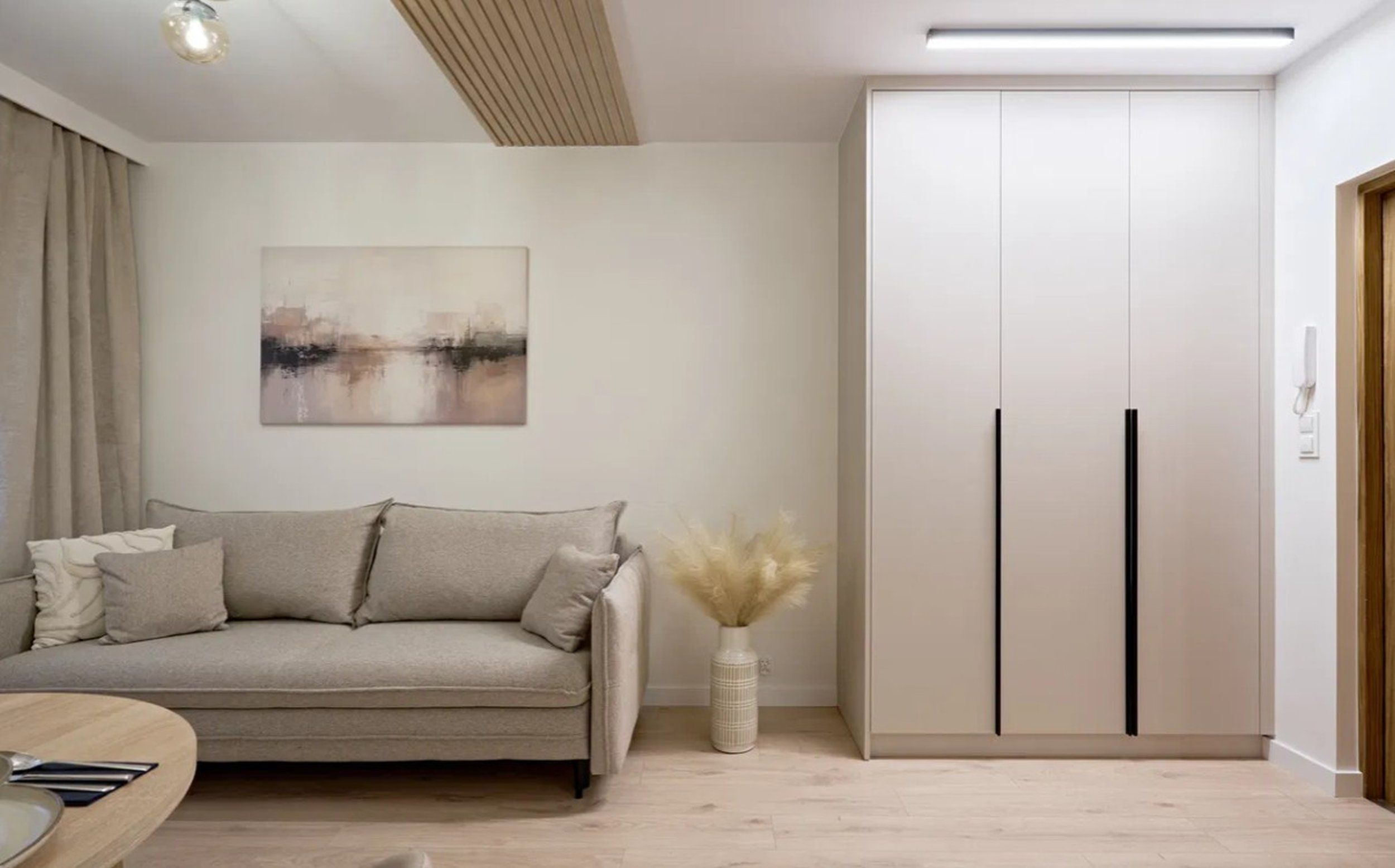 A modern living room with a sofa, a vase with dried plants, and a wardrobe with two doors.