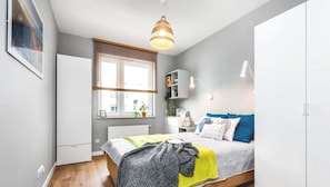 A bedroom with a bed, a window with blinds, a wardrobe, and a hanging light fixture. - Easy Stay Apartments (Gdynia)