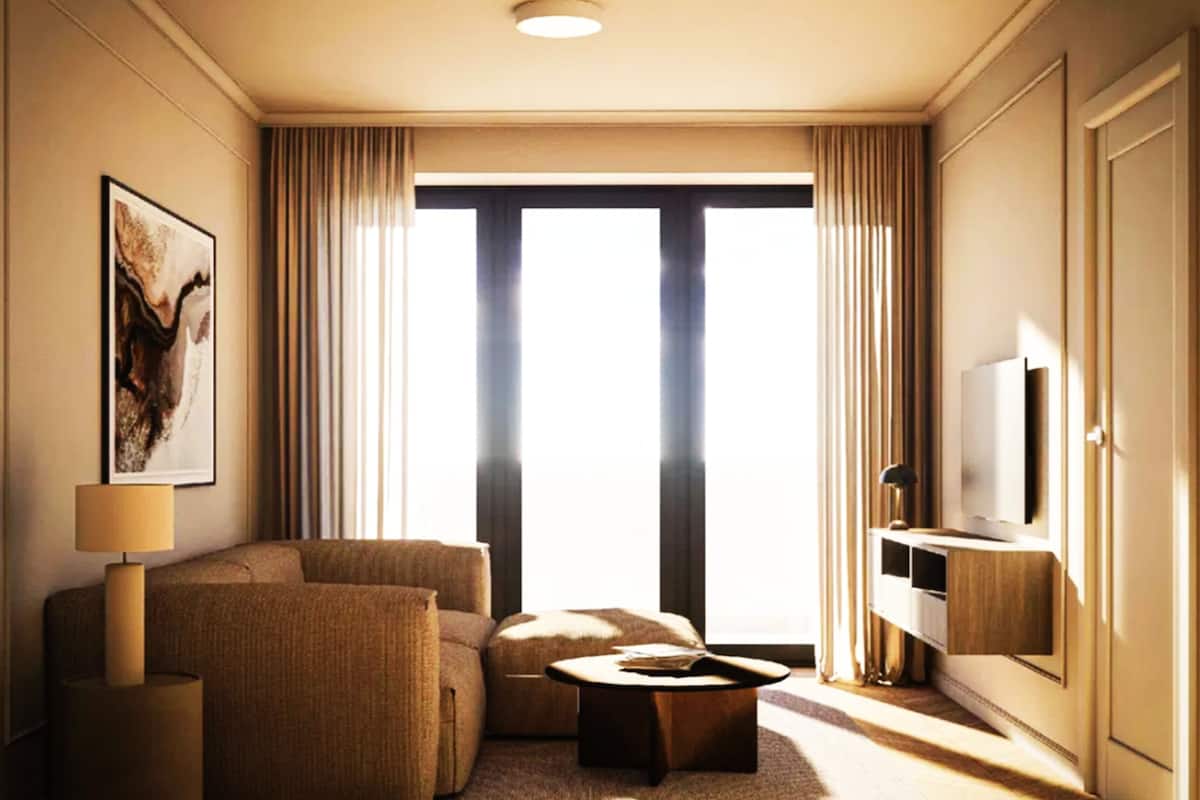 A hotel room with a sofa, armchair, coffee table, TV, and a large window with curtains.