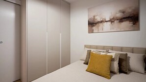 Ein Schlafzimmer mit Bett, Kissen, Kopfteil, Kleiderschrank und einem Bild an der Wand.