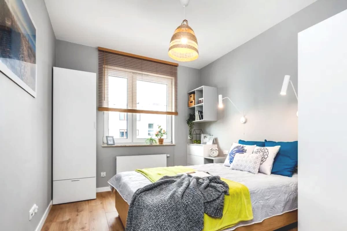 Un dormitorio con cama, ventana con persianas, armario y lámpara colgante.