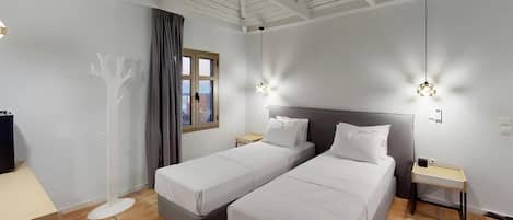 Ein Hotelzimmer mit zwei Einzelbetten, einem Schreibtisch, einer Stehlampe und einem Fenster mit Vorhängen.