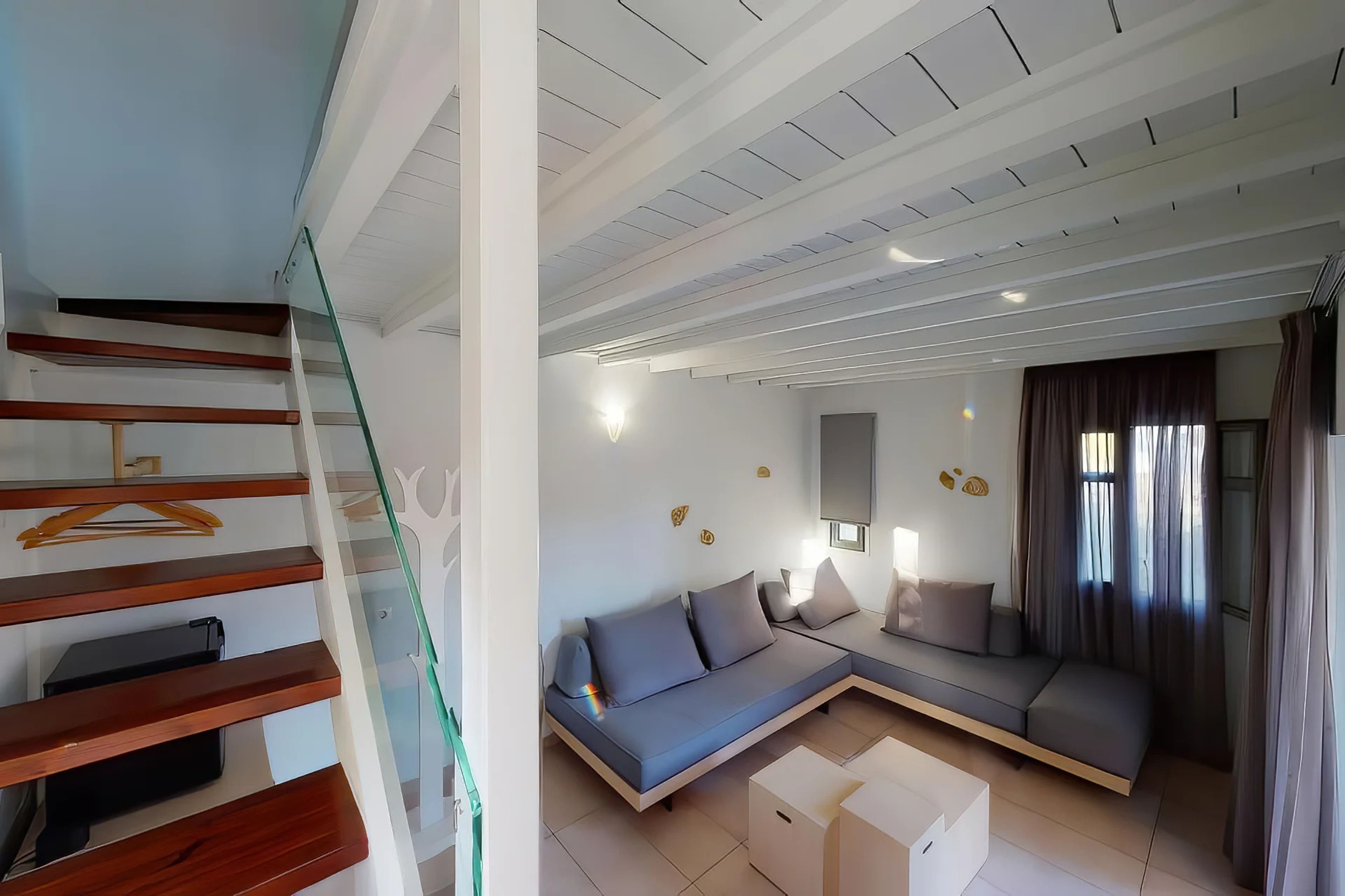 Una sala de estar moderna con un sofá, una escalera de cristal y un televisor de pantalla plana.