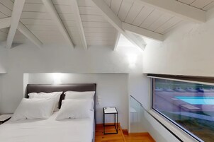 Un dormitorio moderno con cama, mesita de noche y ventana con vistas a una piscina.