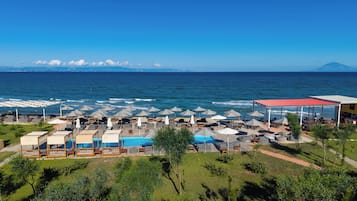 A resort with a pool, beach umbrellas, lounge chairs, and a view of the ocean.